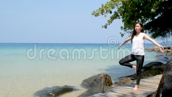 4K暑假期间一个女人站在一条腿上在海上的木桥上练习瑜伽视频的预览图