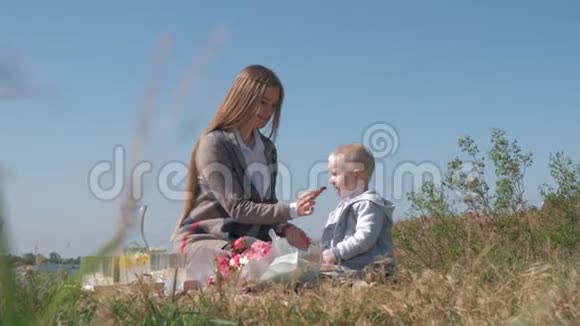 孩子们的食物年轻的妈妈在大自然的家庭野餐中用巧克力糖果喂小孩子视频的预览图