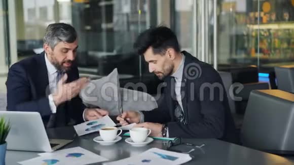 企业家们在咖啡馆开会讨论笔记本电脑图表时争论不休视频的预览图
