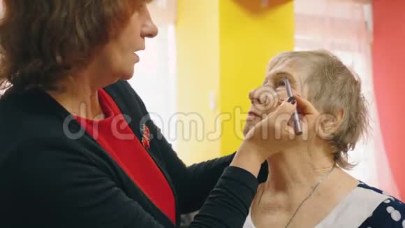老妇人正在给她的朋友化妆应用眼线为眉毛做一个表格视频的预览图