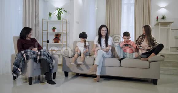 奶奶带着孙子孙女和一个成熟的母亲一起在客厅里玩孩子们正在玩电子游戏视频的预览图