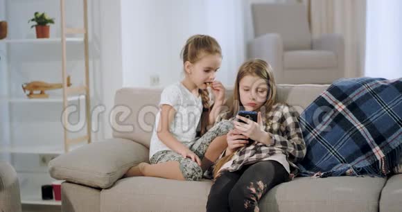 两个小妹妹聚在一起玩电子游戏坐在智能手机上玩视频的预览图
