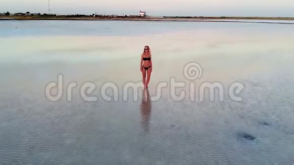 一个穿着黑色泳衣的女孩站在水里看着夕阳一个年轻的女人在盐湖边晒日光浴视频的预览图