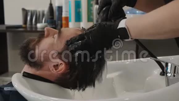 在理发店里把男发梳洗干净美容师在美容院洗手男头理发师洗头视频的预览图