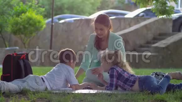现代教育在阳光明媚的大自然中孩子们听着女人读着迷人的书坐在绿草上视频的预览图