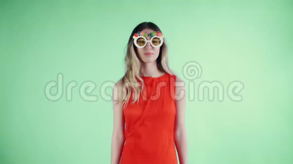 戴着滑稽眼镜的红衣女青年正在绿色背景上跳舞视频的预览图
