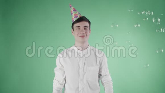 戴着派对帽的年轻人惊讶地在绿色背景上飞泡泡视频的预览图