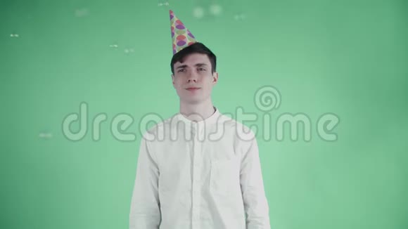 戴着派对帽的年轻人站在绿色背景下的肥皂泡下视频的预览图