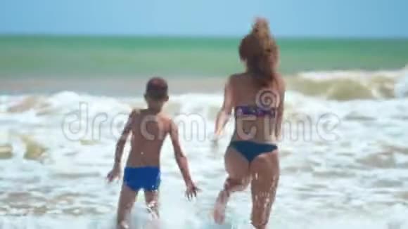 幸福家庭妈妈和宝宝赤脚在湿沙上奔跑后景妈妈和宝宝两只手一起在海滩上奔跑视频的预览图