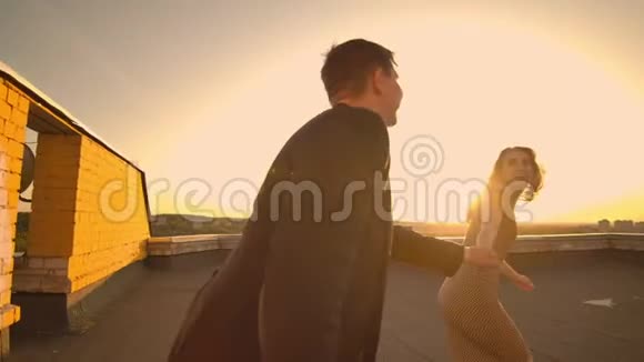 可爱的恋人们在城市背景的日落时分在楼顶上欢笑拥抱着站在视频的预览图