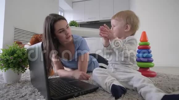 幸福的家庭小可爱的小男孩和小妈妈一起拍手看着躺在地上的笔记本电脑上的动画片视频的预览图