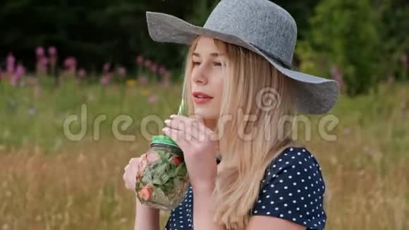 一个年轻漂亮的金发女郎戴着帽子穿着裙子坐在绿色的格子花格子上喝着罐装柠檬水视频的预览图