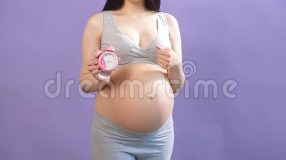 穿内衣的孕妇在肚子里拿着红色闹钟视频的预览图