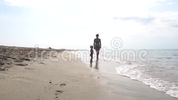 一位母亲和她的孩子在海边散步看着海浪视频的预览图
