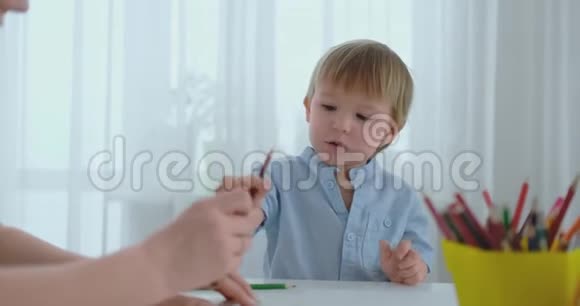 一个穿着蓝色T恤的男孩坐在餐桌旁的厨房里画了一个记号视频的预览图
