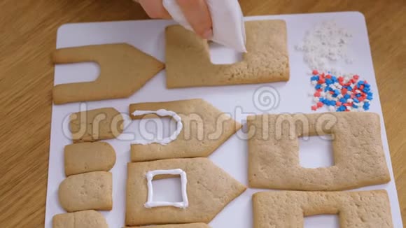 女人手装饰着糖糖甜糖霜饼干用于姜饼屋烹饪自制姜饼屋顶级视频的预览图