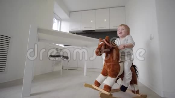 孩子的成长可爱可爱的小男孩骑着毛绒马在家里的房间里微笑视频的预览图
