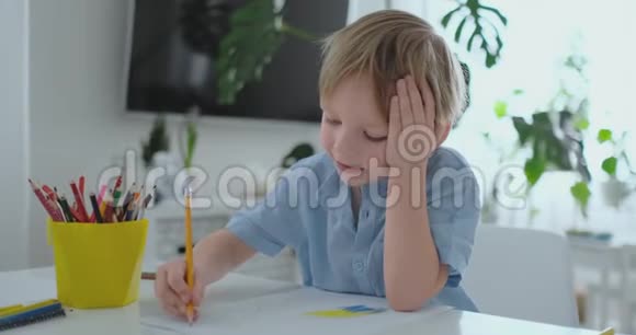 一个穿着蓝色T恤的男孩坐在餐桌旁的厨房里画一支铅笔在做幼儿园的作业视频的预览图