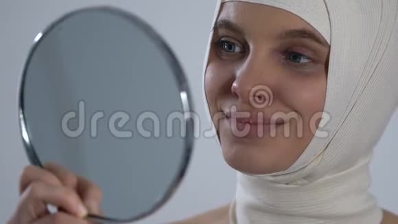 快乐的女孩在头巾照镜子成功的整形手术视频的预览图