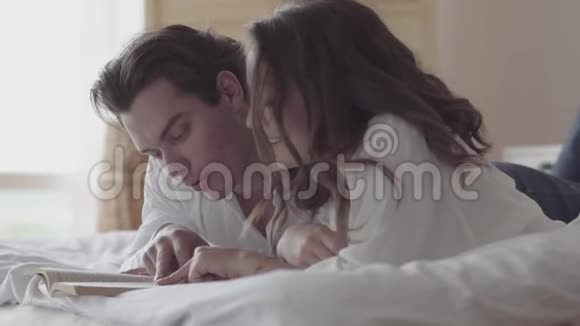 幸福的年轻夫妇躺在床上看书特写美丽的女人和男人在家里睡觉视频的预览图