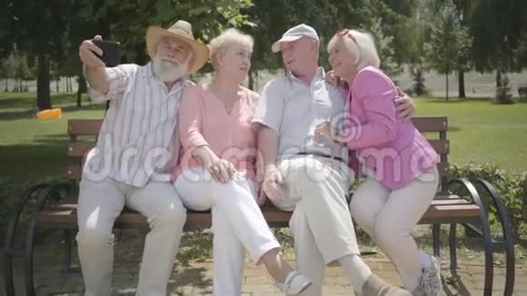 两对可爱的成熟夫妇坐在长凳上老人在公园里拍一张公司的自拍成熟的人视频的预览图