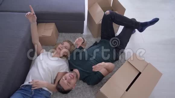 家庭搬迁幸福迷人的男人和女孩躺在地板上的盒子和梦想未来的家庭改善视频的预览图