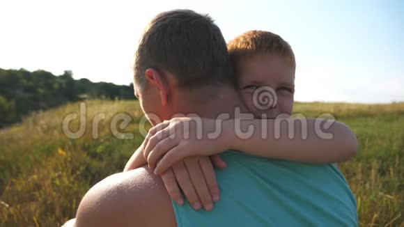 小红发男孩和父亲坐在草地上的绿草上用爱拥抱他快乐的儿子视频的预览图