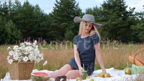 一个年轻漂亮的金发女郎戴着帽子穿着裙子坐在绿色的格子花格子上喝着罐装柠檬水视频的预览图