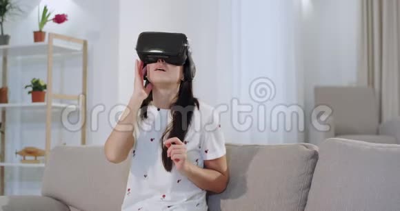 有魅力的女人坐在客厅的沙发上用虚拟现实用手指触摸虚拟选择一个视频的预览图