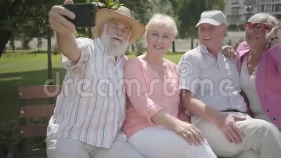 两对可爱有趣的成年夫妇坐在长凳上老人在公园里拍一张公司的自拍成熟成熟视频的预览图