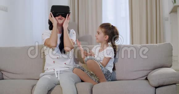 充满魅力的成熟母亲和女儿坐在沙发上用虚拟现实眼镜探索视频的预览图
