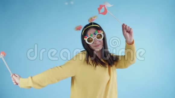 漂亮的年轻女子戴着滑稽的帽子和眼镜独自在蓝色的背景上跳舞视频的预览图