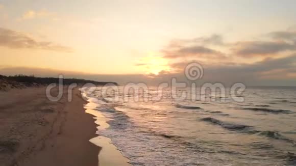 空中观看无人机镜头低飞行在一个废弃的海滩上日落带着滚滚海浪和夕阳的沙岸视频的预览图