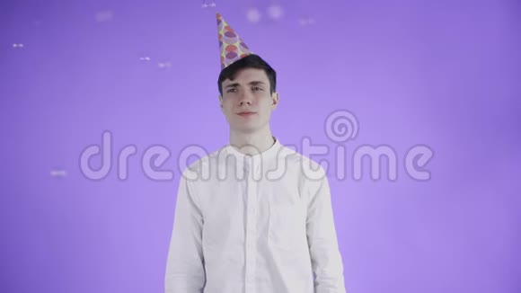 戴着派对帽的年轻人站在紫色背景下的肥皂泡下视频的预览图