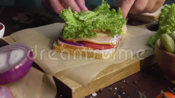 厨师用火腿和沙拉在木板上在光线下完成三明治厨师手完成视频的预览图