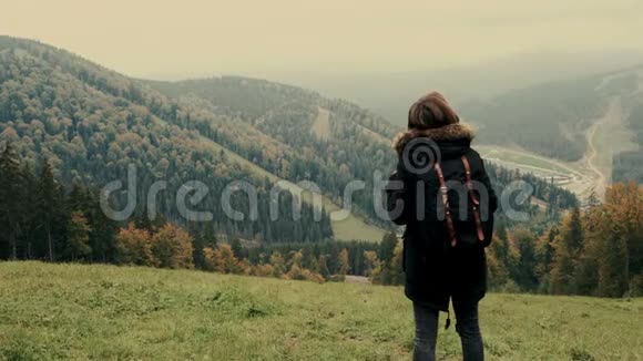 年轻女孩徒步旅行者用常绿针叶树在雾蒙蒙的山景上展示视频的预览图