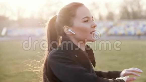 在一个阳光明媚的秋日戴着无线耳机的年轻女孩进行健身运动视频的预览图
