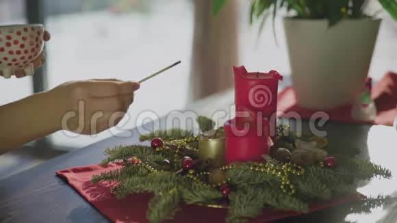手里拿着茶杯的年轻女子点燃了圣诞蜡烛经典新年或圣诞装饰视频的预览图