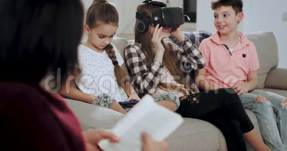 一位老妇人奶奶在沙发上看书而她的孙子们戴着虚拟现实眼镜玩着他们有一个视频的预览图