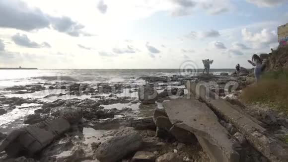 人们在海上看日落海浪冲破海岸上的岩石视频的预览图