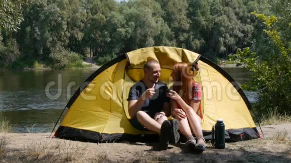 旅游和旅游的概念年轻的幸福夫妇坐在帐篷里看风景喝茶笑着说话视频的预览图