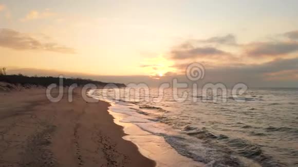 空中观看无人机镜头低飞行在一个废弃的海滩上日落带着滚滚海浪和夕阳的沙岸视频的预览图