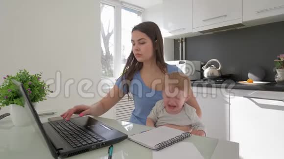 结合工作和父母母亲和哭泣的小儿子一边工作在笔记本电脑和手机交谈视频的预览图