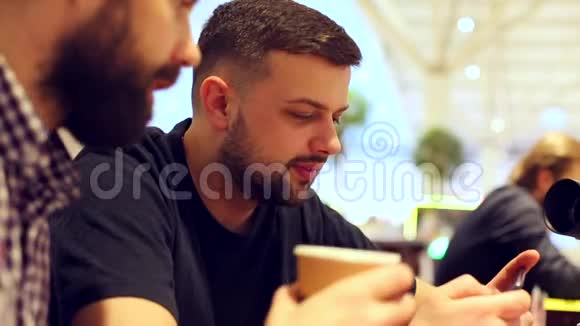 一个特写的年轻人在电话里看视频喝咖啡他们在电话里聊天看视频视频的预览图