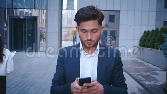 年轻的商人在大城市商业区街上散步时使用智能手机穿着得体大人物视频的预览图