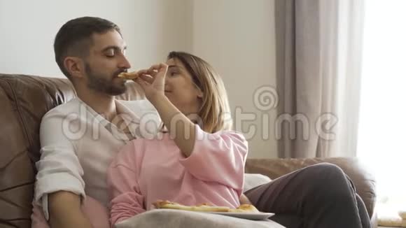 一位成年女性坐在皮革沙发上用美味的自制比萨饼喂丈夫幸福的夫妻浪漫视频的预览图