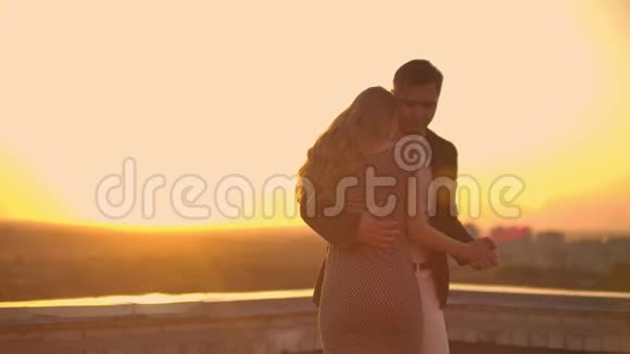 两个情人在日出日落时在俯瞰城市的摩天大楼上拥抱跳舞浪漫的场景视频的预览图