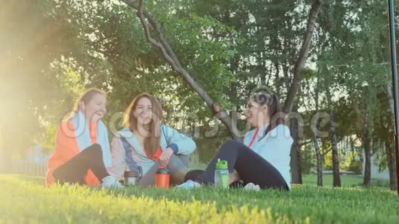 三个朋友在晨跑后坐在草地上他们笑着说话视频的预览图