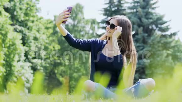 漂亮的女人在智能手机上自拍城市公园的花费时间视频的预览图