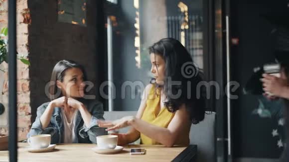 年轻女子在咖啡馆里用智能手机和女服务员聊天视频的预览图